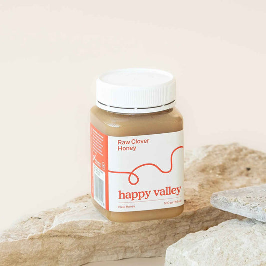 Jar of Happy Valley Honey Clover Field Gourmet & Raw Honey showing golden honey with a floral background