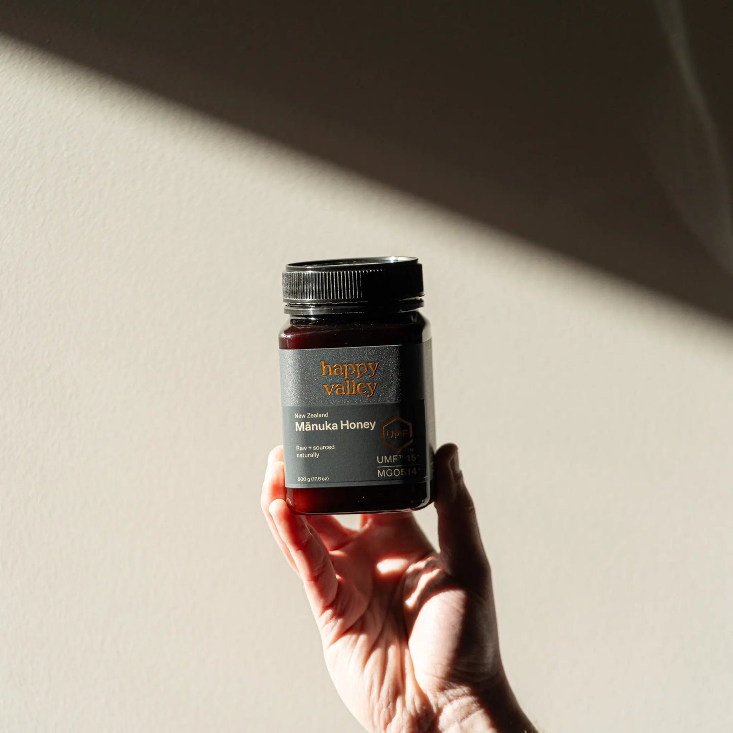 Jar of Happy Valley Honey Manuka Honey UMF® 15+ with golden honey drizzled on a wooden surface.
