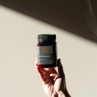 Jar of Happy Valley Honey Manuka Honey UMF® 15+ with golden honey drizzled on a wooden surface.
