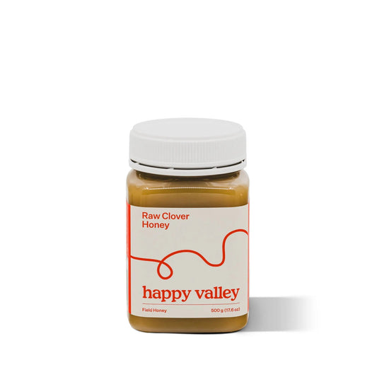 Glass jar of Happy Valley Honey Clover Field Gourmet & Raw Honey with golden honey drizzling from the lid.