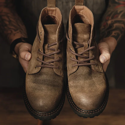 Brown leather boots held by a person with tattooed arms.
