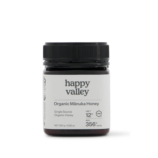 Organic Manuka Honey UMF® 12+ jar from Happy Valley Honey, showcasing golden, thick honey with a white label and wooden honey dipper